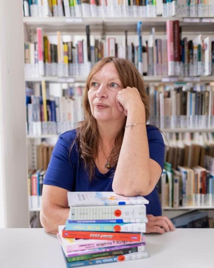 Portrait de Christel Hortz accoud&eacute;e &agrave; une pile de livres jeunesse, dans une biblioth&egrave;que.